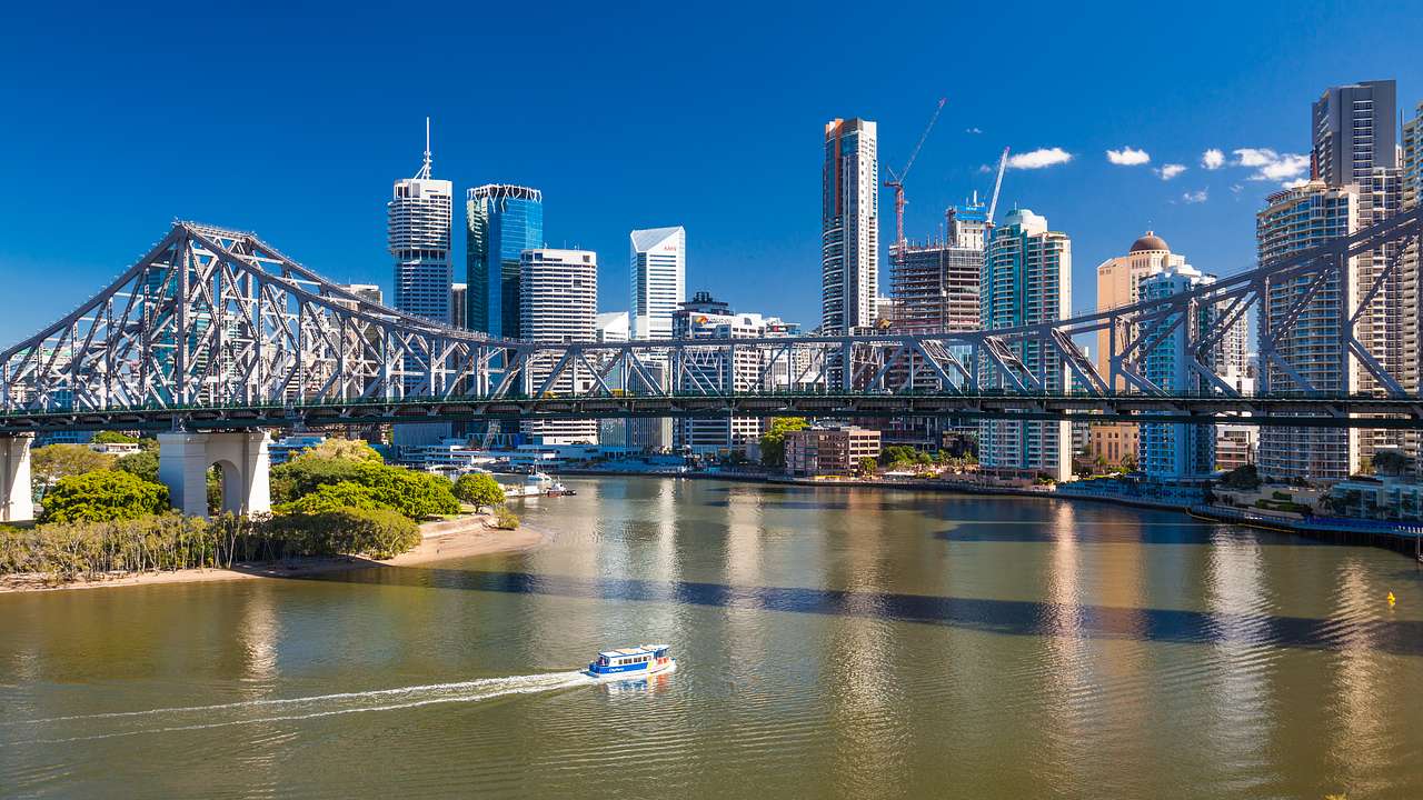 Sunny skyline of skyscrapers behind a bridge across a still body of water and a boat