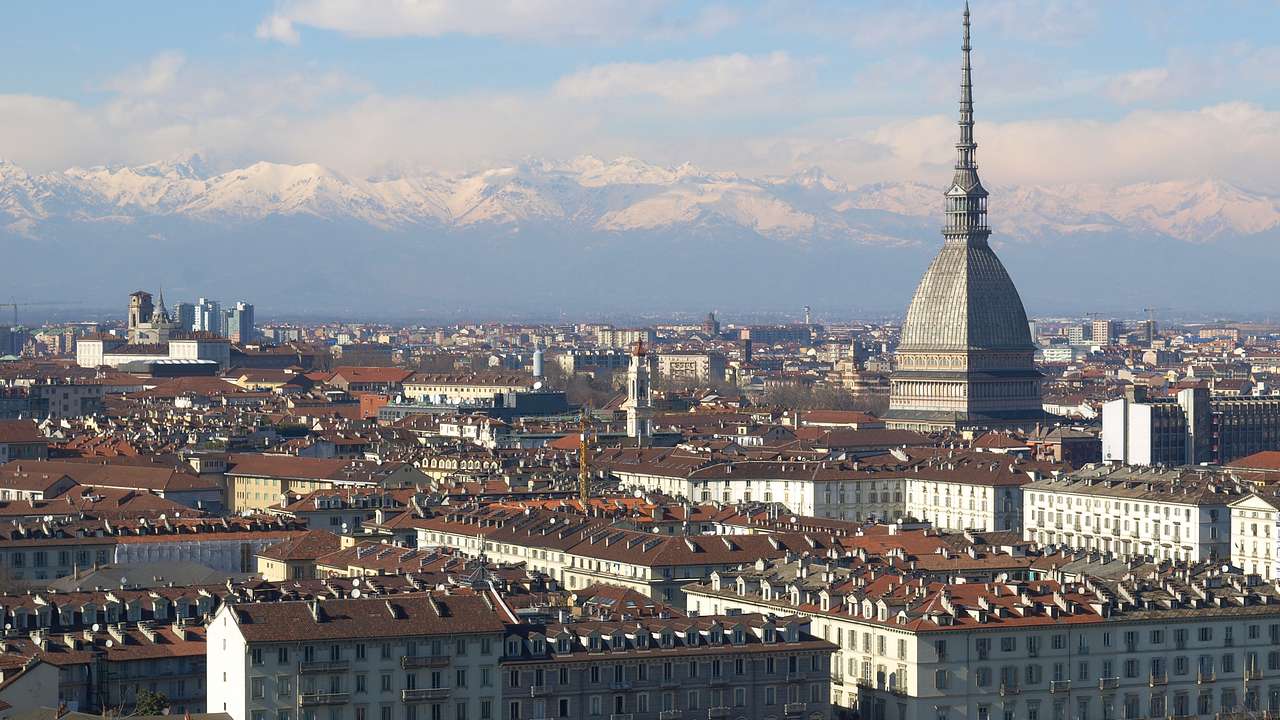 Cityscape of red-roofed buildings dominated by a spired dome against snowy mountains