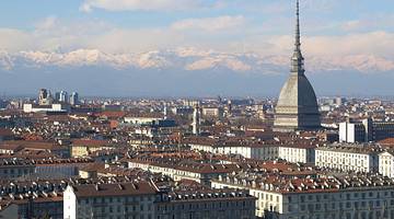 Cityscape of red-roofed buildings dominated by a spired dome against snowy mountains
