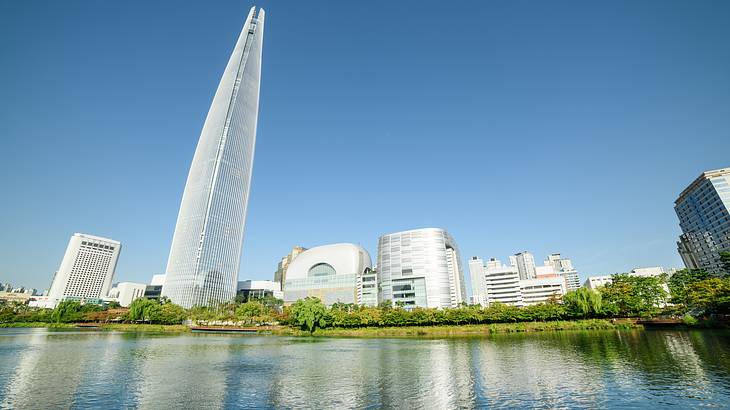 Sunny skyline of buildings and a pointy structure towering over a calm body of water