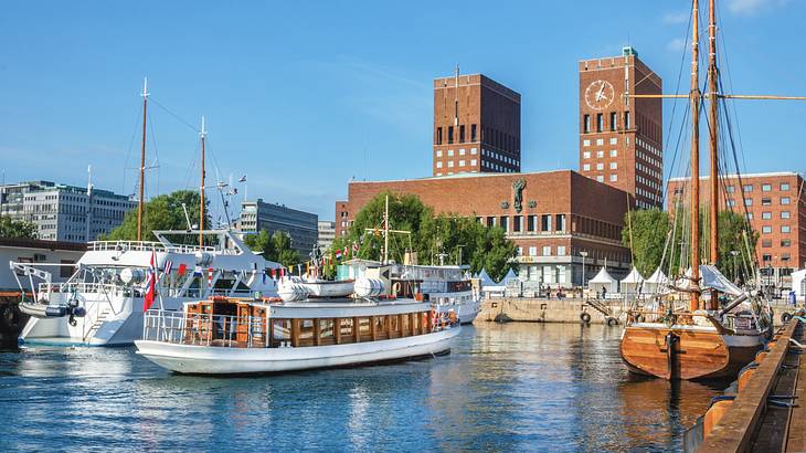 Boats in a harbor in front of a large wide brick building with two tall towers