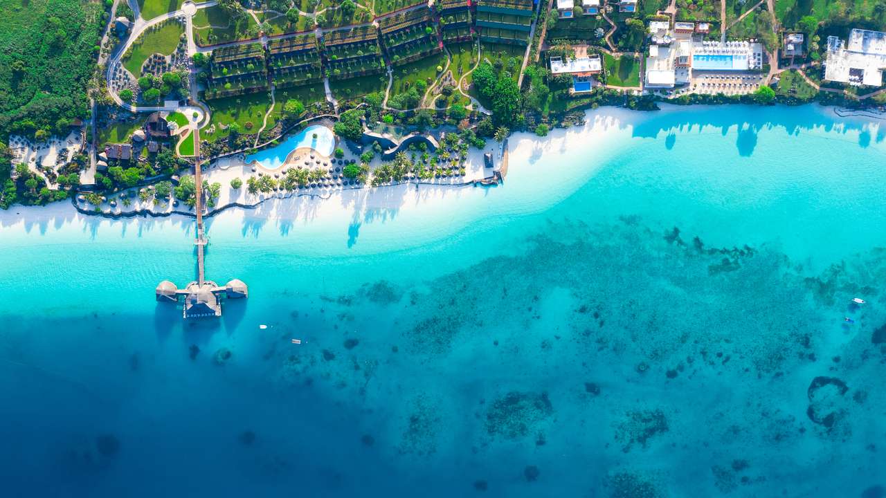 Bird's eye view of a blue sea with a white sandy beach, a resort, and lush greenery