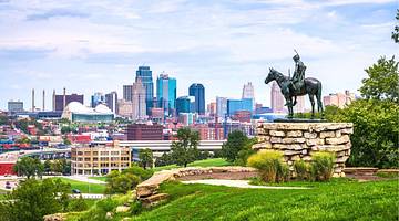 A city skyline at the back with a man on a horse statue on a hill in front