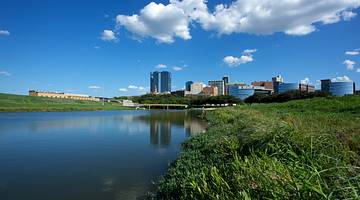 A city skyline far away with grass and water in front on a partly cloudy day