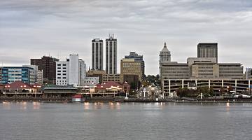 A city skyline with buildings behind water, on a cloudy day