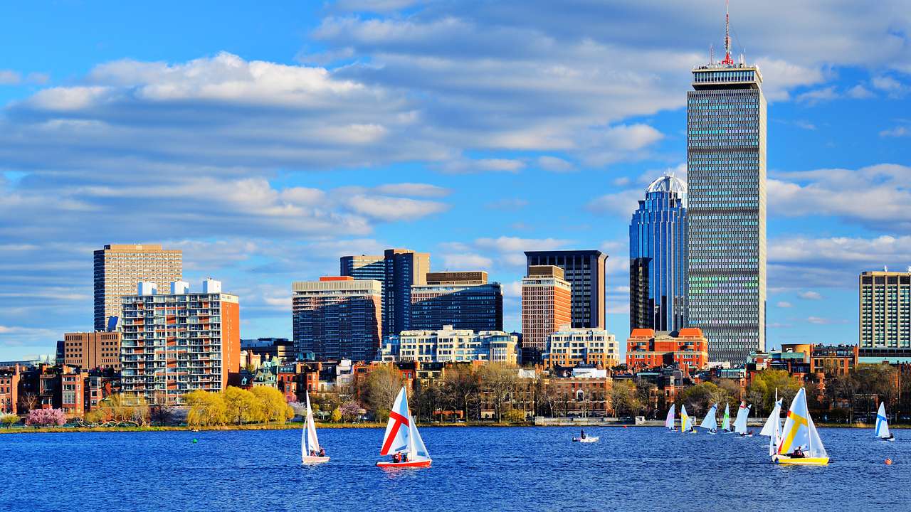 City skyline with a partly cloudy sky above and sailboats on water in front