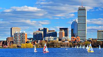 City skyline with a partly cloudy sky above and sailboats on water in front