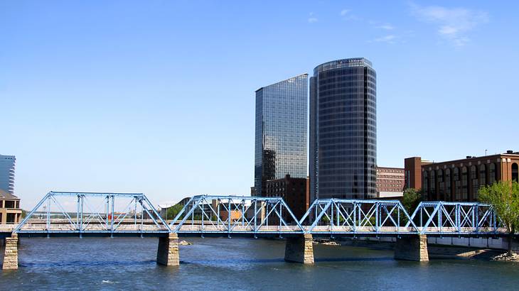 A blue bridge across water with some concrete and glass buildings on the right