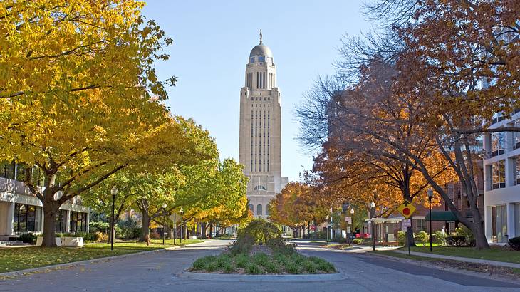 A paved road with a garden in the middle in front of a tall white domed building