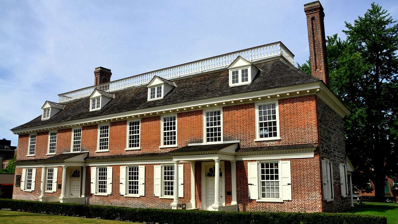 A rectangular red brick manor with a chimney, surrounded by green grass and trees