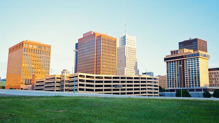 A city skyline with tall buildings and green grass in front on a clear blue day