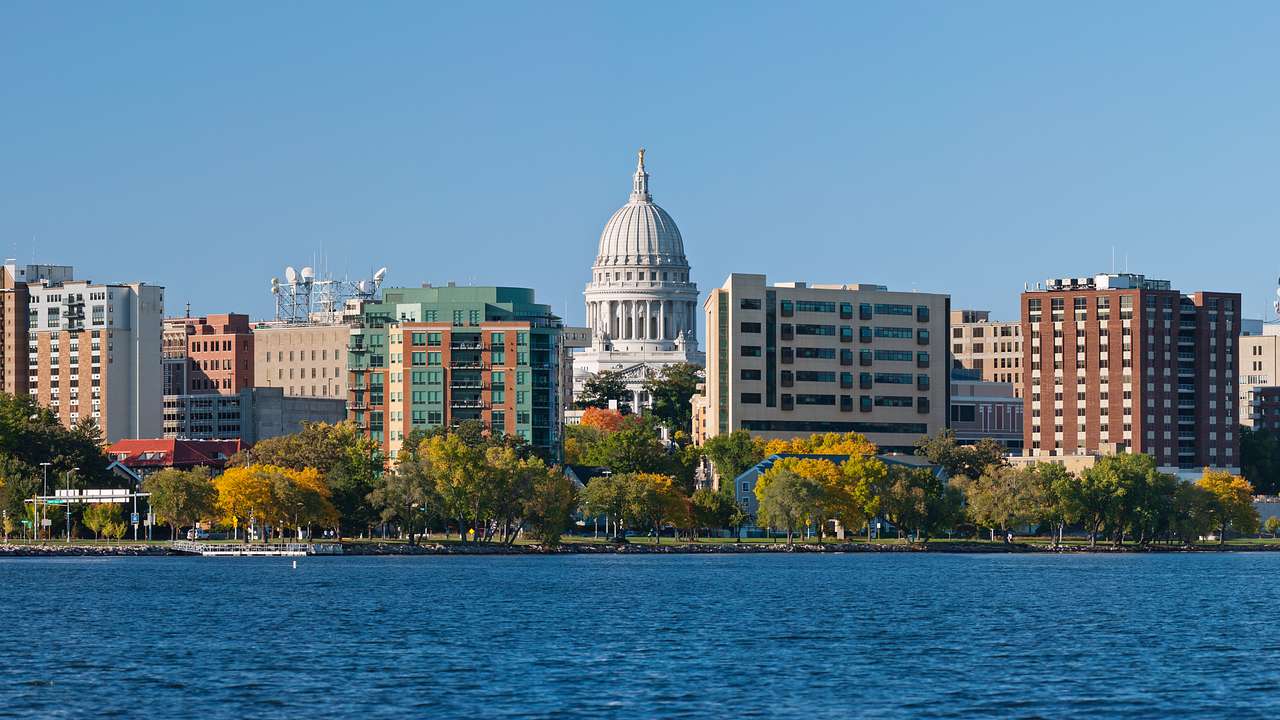 A city skyline full of buildings, a state capitol, and trees, with water in front