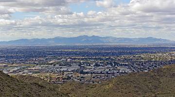Looking over a flat town from a grassy hill with a mountain range at the back