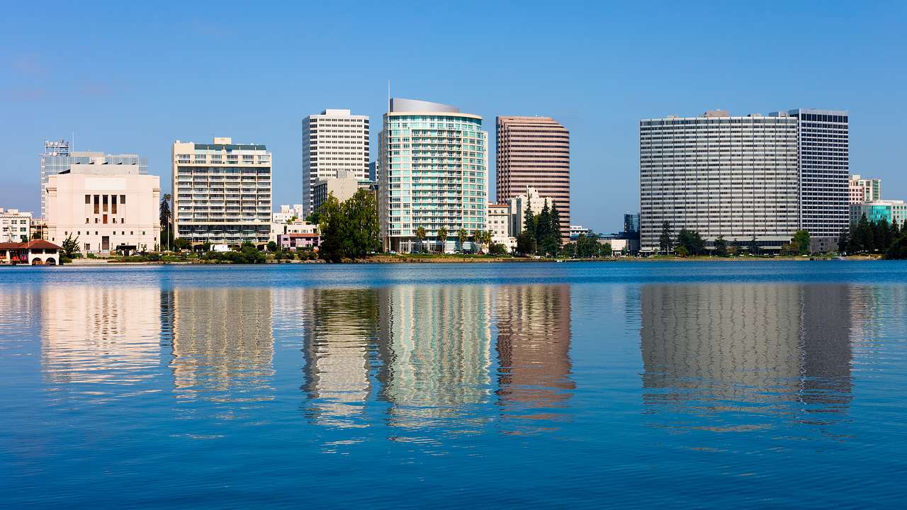 A city skyline with glass buildings reflected in water on a clear blue day