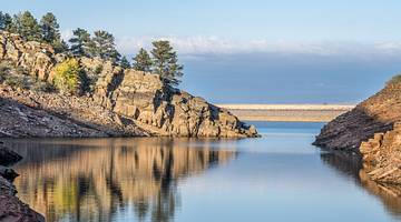 A peaceful reservoir with still water and rocky cliffs with green trees around