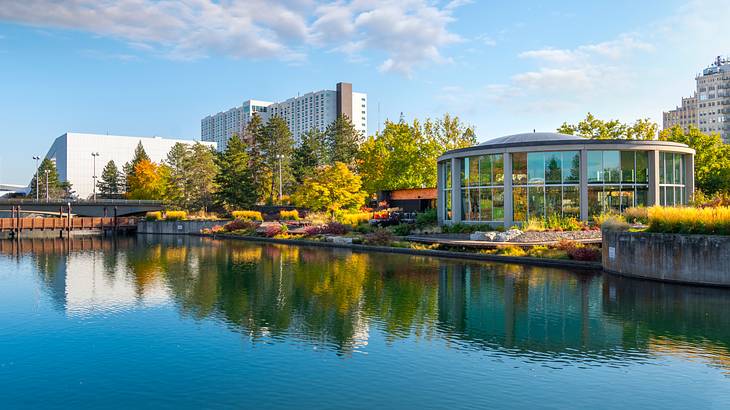 A large circular glass building along a riverside lined with yellow and brown trees