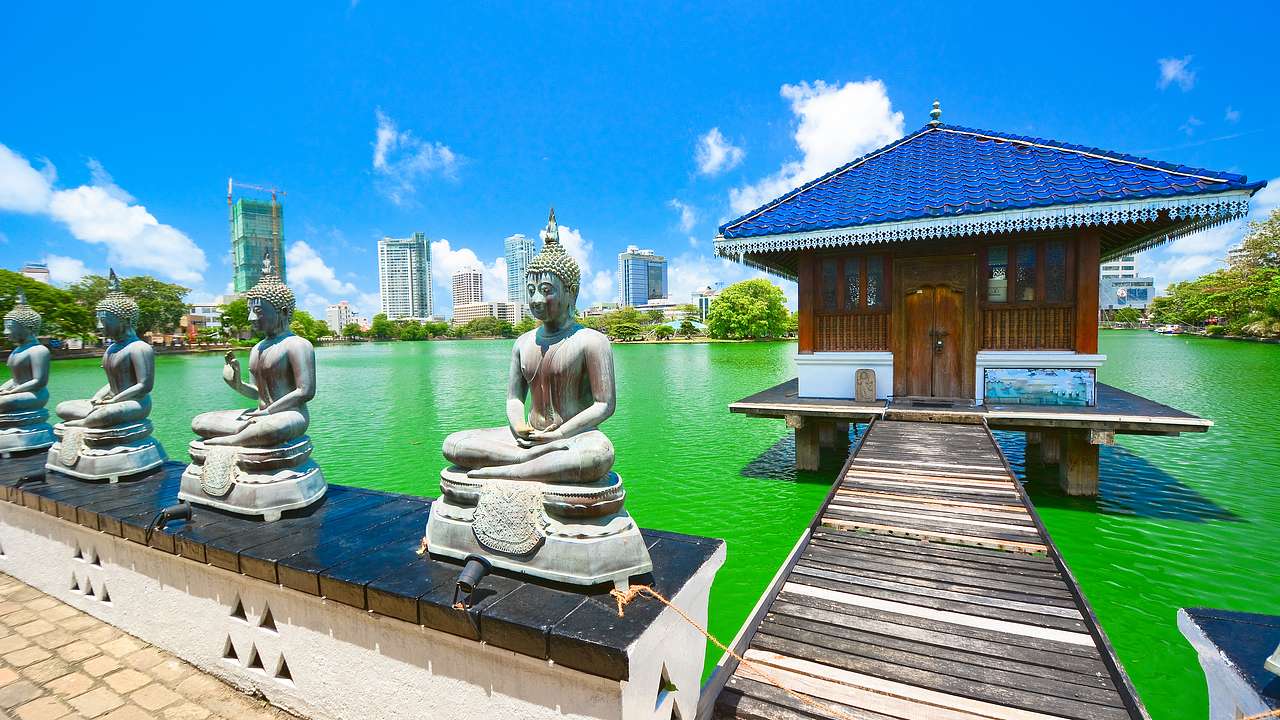Buddha statues next to walkway of house on body of water against a sunny city skyline