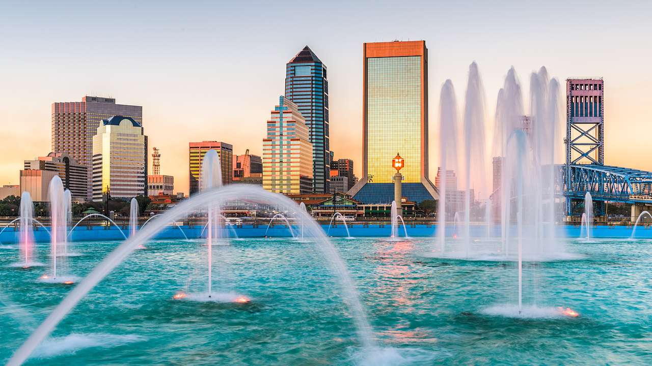 Water fountains spurting water into the air in front of a city skyline at sunset