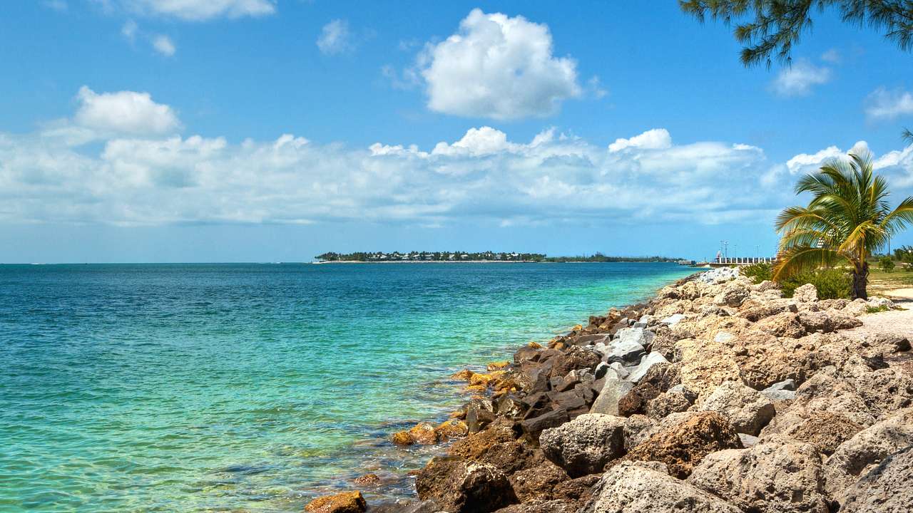 A rocky coastline with bright blue, clear water and white fluffy clouds above