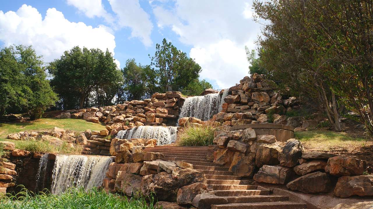 A stone staircase with rocks and grass beside a cascading waterfall system