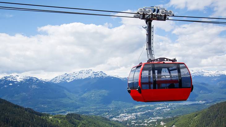 A red tram high above in the sky over a green mountainous area on a nice day