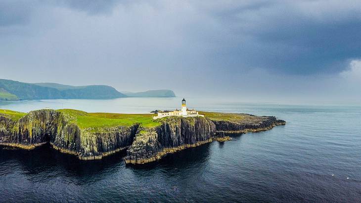 A white lighthouse on the cliffside of a green grassy island surrounded by an ocean