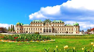A palace building with Baroque architecture overlooking green grass and flowers