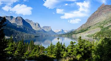A mountain range at the back with a lake and green pine trees in front