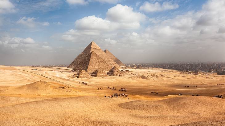 A number of pyramid monuments surrounded by a desert under a partly cloudy sky