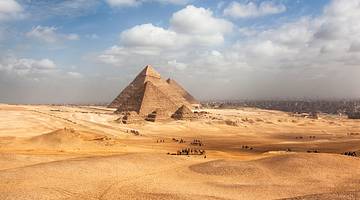 A number of pyramid monuments surrounded by a desert under a partly cloudy sky