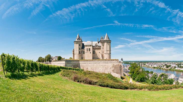 A large stone tower with two tall towers on a hill overlooking a town by a river