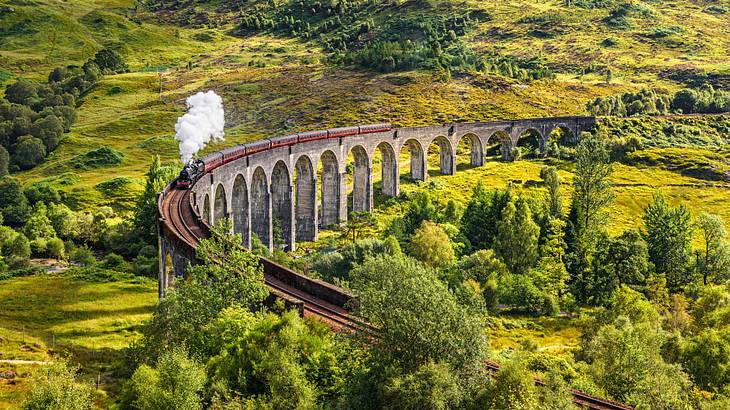 A steam engine passing over a viaduct in a green mountainous area