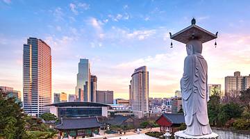 A tall statue of a man overlooking a temple against a modern skyline