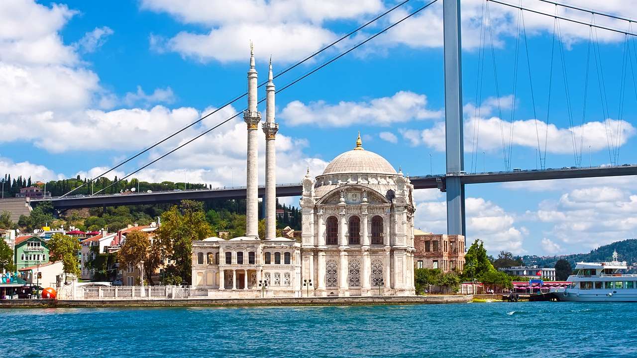A white mosque by the blue water against a suspension bridge