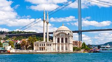 A white mosque by the blue water against a suspension bridge