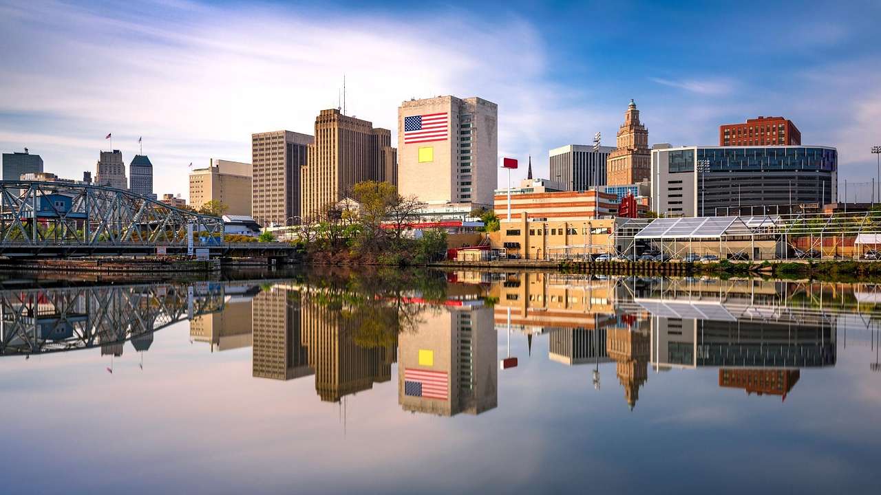 A city skyline with varying buildings and a steel bridge reflected in water