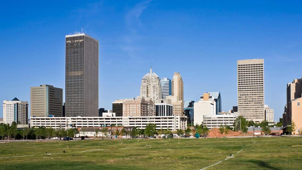 A city skyline with buildings against blue sky and behind a green field