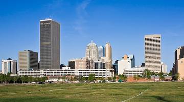 A city skyline with buildings against blue sky and behind a green field