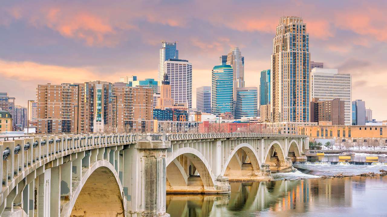 An arched bridge across water in front of a skyline full of skyscrapers at the back