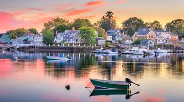 Quaint houses along a waterfront with small boats moored in front at dusk