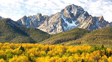 Rugged snow-capped mountains overlooking hills covered with green trees