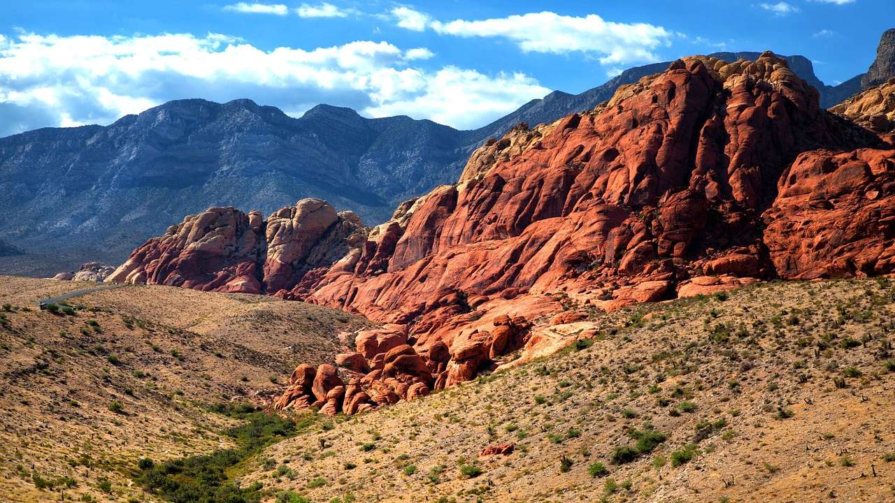 A red rock structure surrounded by brown and green grass, against a rugged mountain