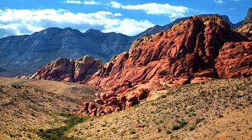 A red rock structure surrounded by brown and green grass, against a rugged mountain