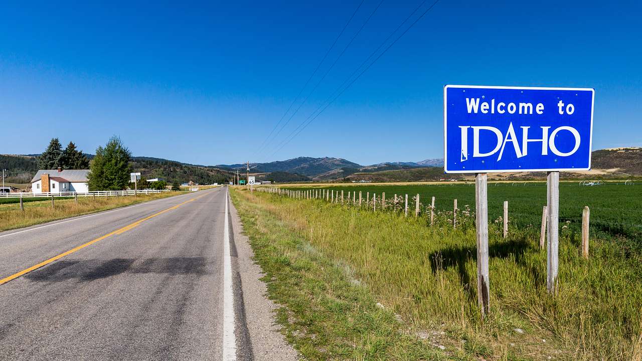 A blue and white "Welcome to Idaho" sign on the right of a grassy highway