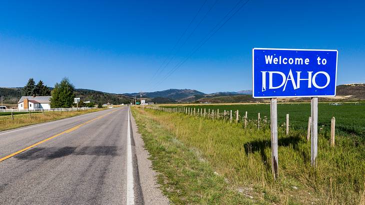 A blue and white "Welcome to Idaho" sign on the right of a grassy highway