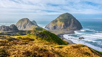 Coastal hilly landscape with sandy beach, waves and large boulders