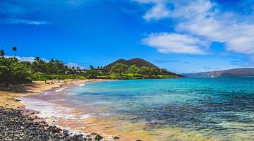 A beach with green trees against a black hill, overlooking the blue sea