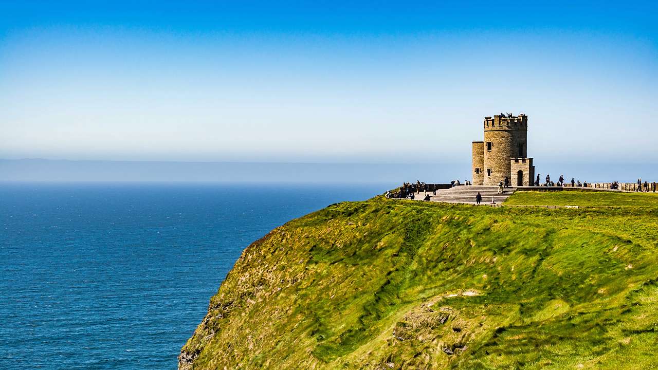 A stone castle with a tower on the edge of a high cliff top overlooking a blue ocean